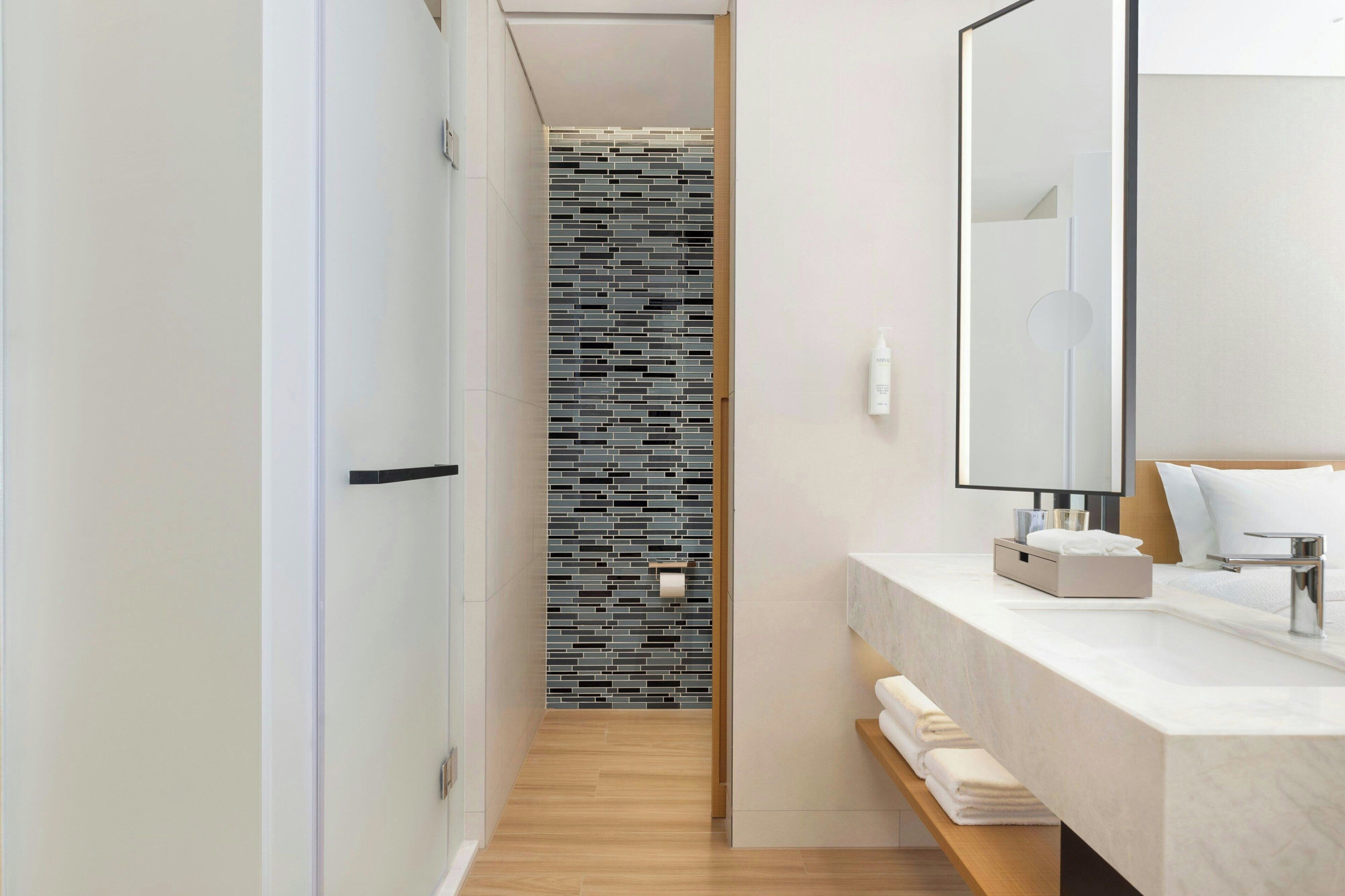 A modern bathroom with a shower, a large mirror, and a marble sink.