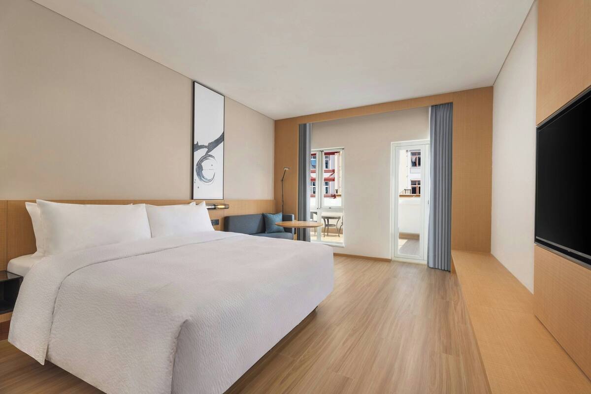 Habitación de hotel con una cama grande, un escritorio, una silla, un televisor y vistas al exterior.