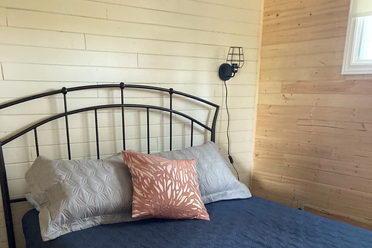 Una cama con colcha azul, dos almohadas y una manta escocesa, junto a un cabecero de madera.