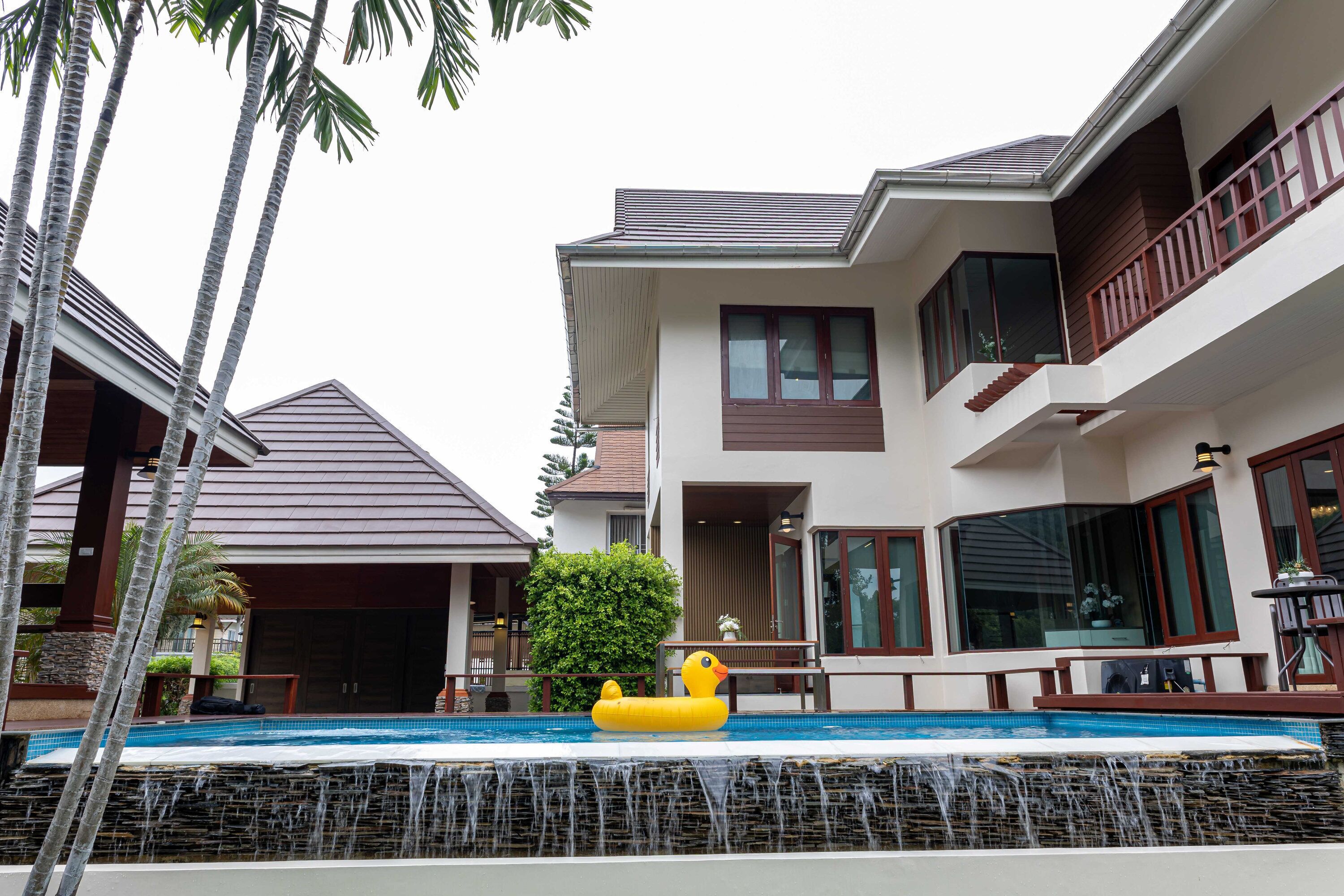 Een modern herenhuis met zwembad, een houten terras en een waterval.