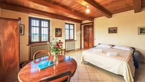 Ein Zimmer mit Holzboden, einem Bett mit weißer Bettwäsche, einem Esstisch mit Stühlen und einer Vase mit Blumen.