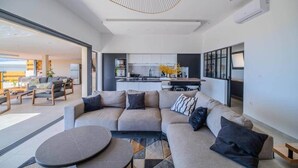 Uma sala de estar moderna com um amplo sofá em formato de L, uma mesa de centro redonda e uma área de jantar ao fundo.