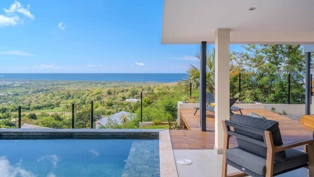 Uma área moderna com piscina ao ar livre, vista para o oceano e paisagem exuberante.