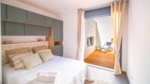 Quarto com cama, mesas de cabeceira, guarda-roupa e varanda com cadeira e planta.