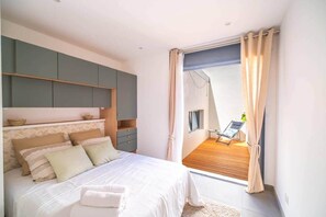 Ein Schlafzimmer mit Bett, Nachttischen, einem Kleiderschrank und einem Balkon mit Stuhl und Pflanze.