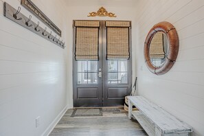 A hallway with a dark double door, a bench, a wall-mounted mirror, and a sign above the door. - Coastal Modern Oasis with Private Pool, Golf Cart, Putt-Putt | Steps to the Gulf (Panama City Beach)