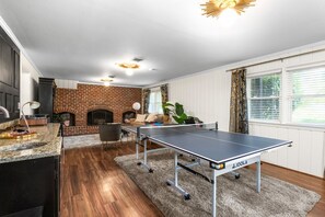 En stue med et ping-pong bord, pejs og et køkkenområde med vask og bordplade.