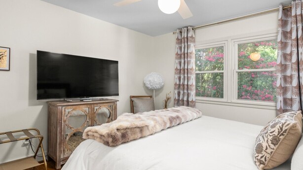 A bedroom with a bed, a television, a wooden cabinet, and a window with curtains.