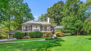 A two-story house with a covered porch, a well-maintained lawn, and mature trees in the background.