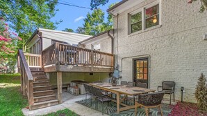 A two-story house with a balcony, a patio with a table and chairs, and a brick exterior.