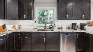 A kitchen with dark wood cabinets, a stainless steel dishwasher, and a window with a view of greenery.
