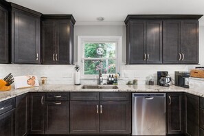 A kitchen with dark wood cabinets, a stainless steel dishwasher, and a window with a view of greenery.