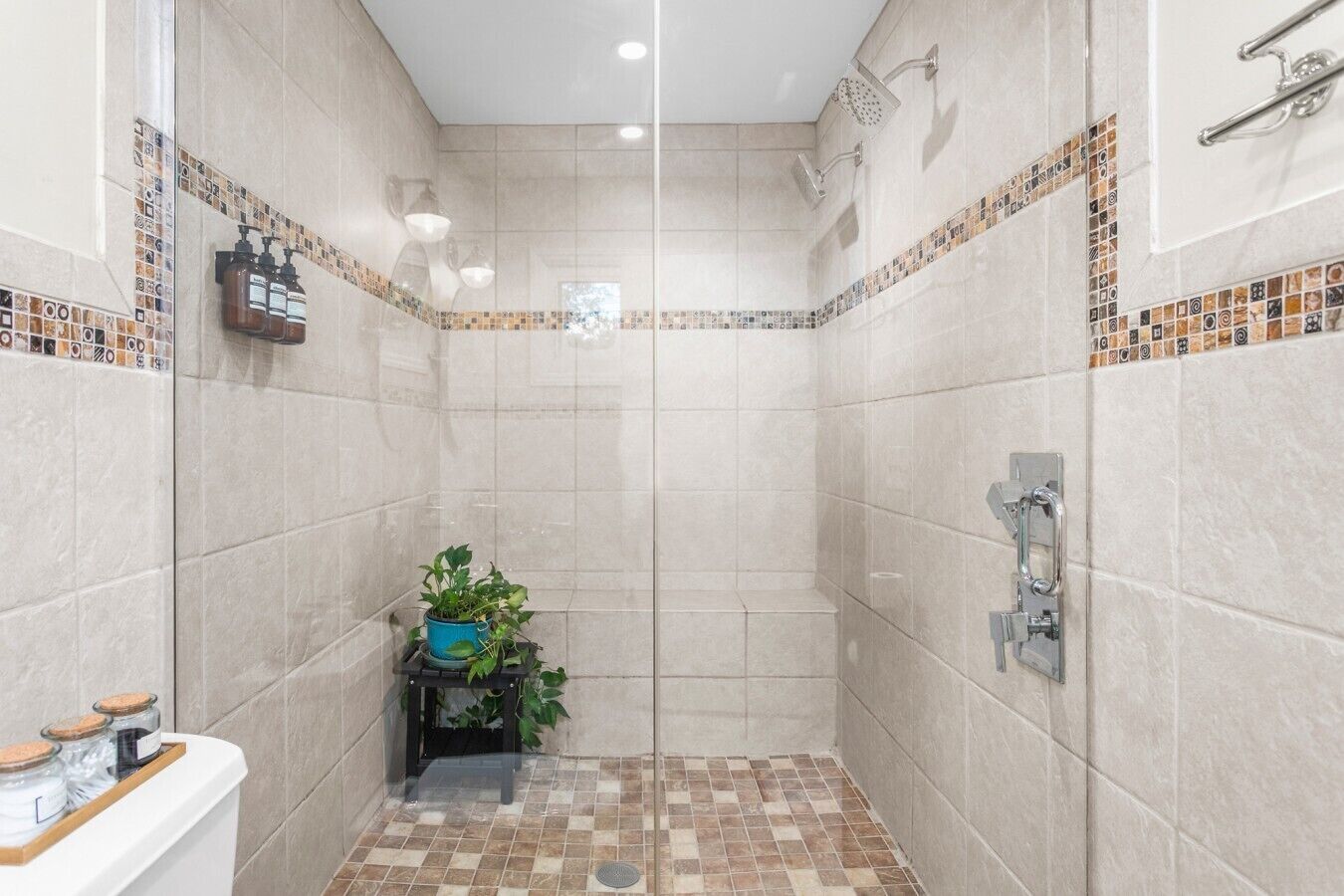 Un espace douche avec des murs carrelés, une pomme de douche et un petit banc agrémenté de plantes.