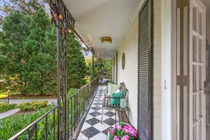 Un porche cubierto con piso a cuadros, mobiliario exterior y vistas a un jardín.