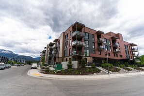 Un immeuble résidentiel à plusieurs étages, doté de balcons, d’un espace de stationnement et situé dans un cadre montagneux.
