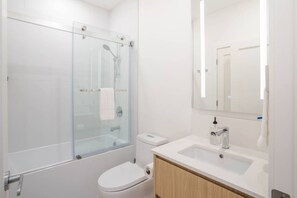 Uma casa de banho moderna com chuveiro em cabine de vidro, sanita e lavatório com espelho em cima.