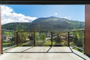 Un balcon offrant une vue dégagée sur un paysage montagneux, des maisons et une zone boisée.