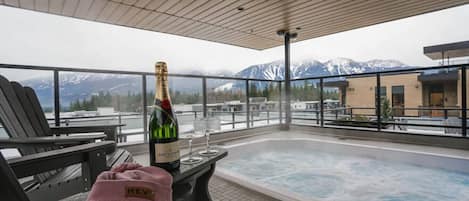 Un jacuzzi con vistas a la montaña, una botella de champán y una toalla rosa sobre una mesa.