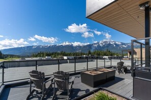 Terraço no telhado com área de estar externa, lareira e vista para montanhas cobertas de neve.