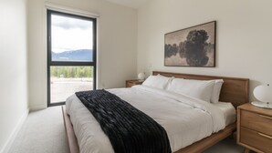 Ein Schlafzimmer mit Bett, Nachttisch, Lampe, Fenster und einem Gemälde an der Wand.