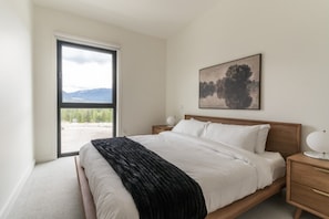 Ein Schlafzimmer mit Bett, Nachttisch, Lampe, Fenster und einem Gemälde an der Wand.