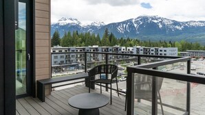 Ein Balkon mit Tisch und Stühlen mit Blick auf ein Wohngebiet, das Gebäude und schneebedeckte Berge zeigt.