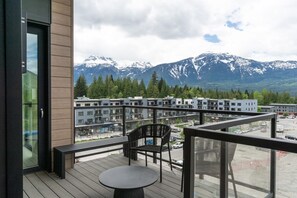 Ein Balkon mit Tisch und Stühlen mit Blick auf ein Wohngebiet, das Gebäude und schneebedeckte Berge zeigt.
