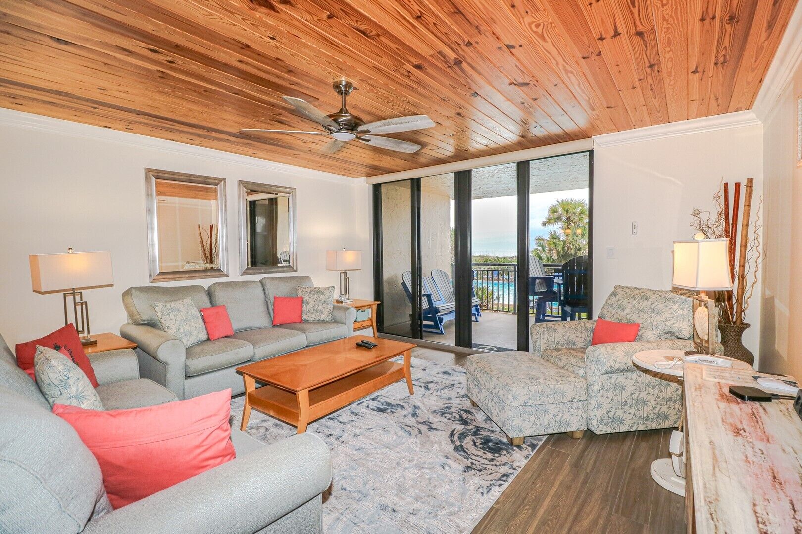 A spacious living room with a wooden ceiling, a large sofa set, a coffee table, and a view of the ocean through large sliding doors.