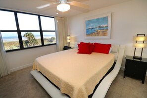 A bedroom with a large bed, a ceiling fan, a window with a view of the beach, and two bedside tables with lamps. - Premium, Remodeled Direct Oceanfront Two Bedroom Condo--Barefoot Trace 207 (St. Augustine)