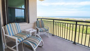 Un balcon avec deux chaises à rayures et une petite table, donnant sur une plage.