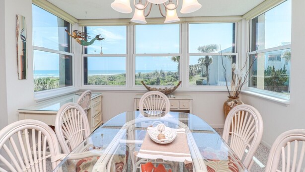 Un espace repas avec une table en verre, des chaises blanches et une vue sur l’océan.