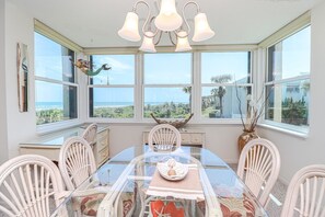 Un espace repas avec une table en verre, des chaises blanches et une vue sur l’océan.