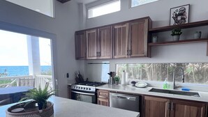 Una cucina moderna con mobili in legno, piano cottura a gas e lavastoviglie. Una finestra offre vista sull'oceano.