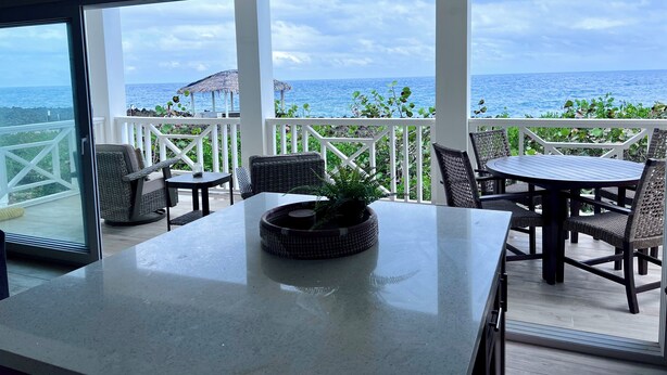 Un balcone con vista sull'oceano, arredato con sedie in vimini e un tavolo, e una ventola a soffitto.