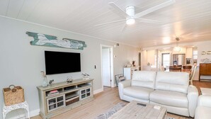 A living room with a TV, white sofa, wooden coffee table, and a ceiling fan. - Island South 2-Beautiful Oceanfront Ground Floor, Two Bedroom Condo (St. Augustine)