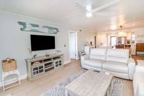 A living room with a TV, white sofa, wooden coffee table, and a ceiling fan. - Island South 2-Beautiful Oceanfront Ground Floor, Two Bedroom Condo (St. Augustine)