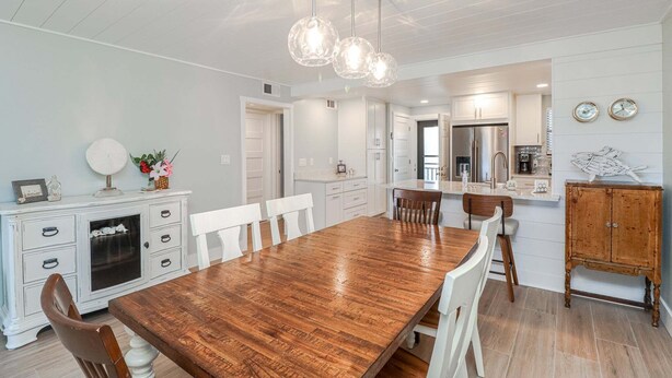 A dining area with a wooden table, white chairs, a white cabinet, and pendant lighting. - Island South 2-Beautiful Oceanfront Ground Floor, Two Bedroom Condo (St. Augustine)