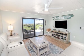 A living room with a sofa, coffee table, TV, and a sliding glass door leading to an outdoor patio. - Island South 2-Beautiful Oceanfront Ground Floor, Two Bedroom Condo (St. Augustine)