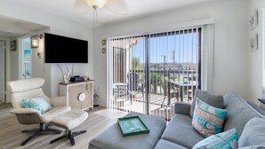 Een moderne woonkamer met een bank, een fauteuil, een flatscreen televisie en een plafondventilator.
