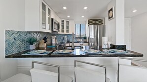 Een moderne keuken met witte kastjes, een backsplash van mozaïektegels in een herringbone patroon, en een centraal eiland met barstoelen.