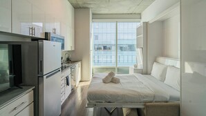 A modern hotel room with a bed, a kitchenette, and a large window offering a city view. - Kenect 2310 (Phoenix)
