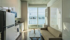 A modern kitchen with a refrigerator, stove, and sink. There is a sofa and a coffee table in the living area. - Kenect 2310 (Phoenix)