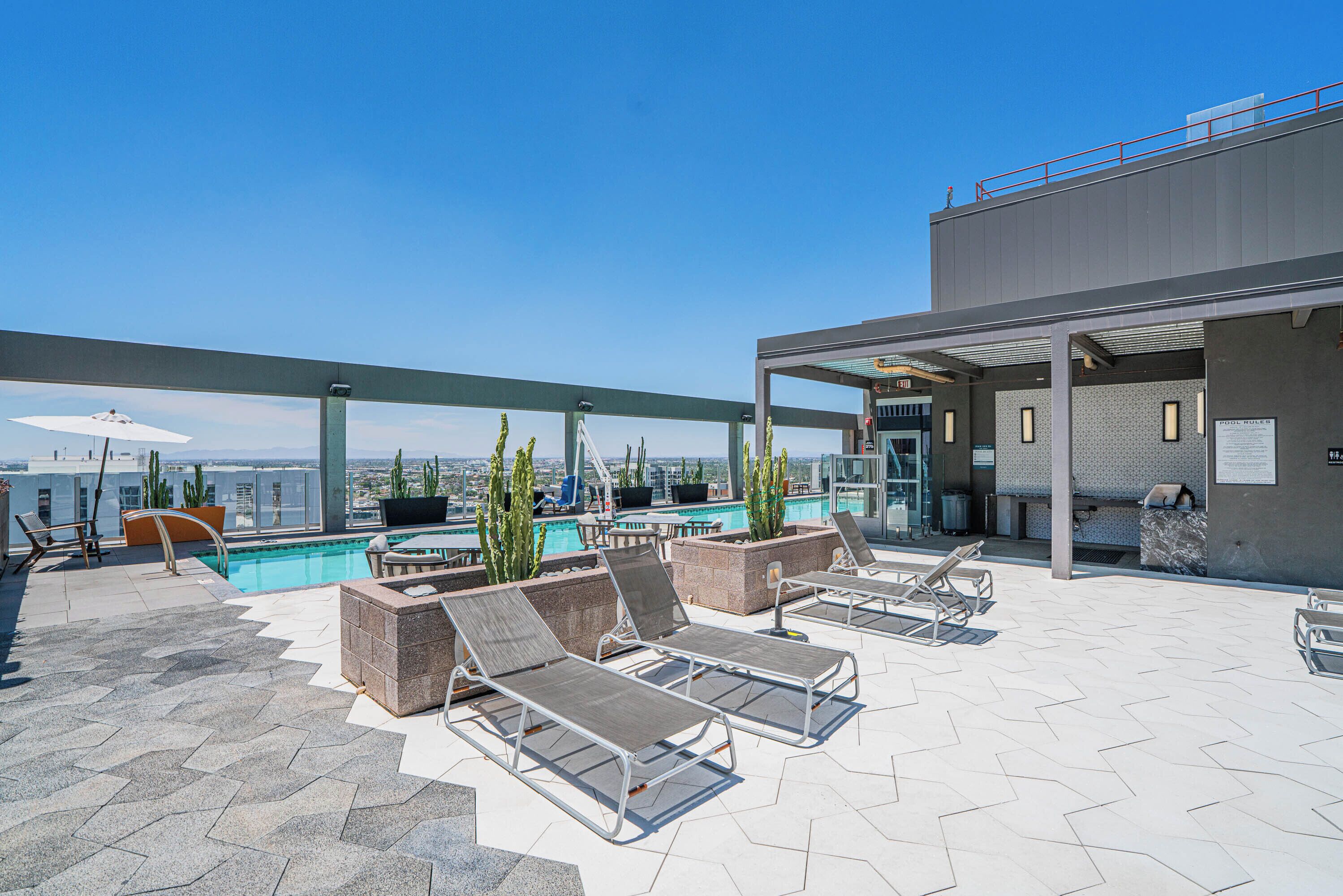 A rooftop pool area with lounge chairs, a pool, and a view of the city.