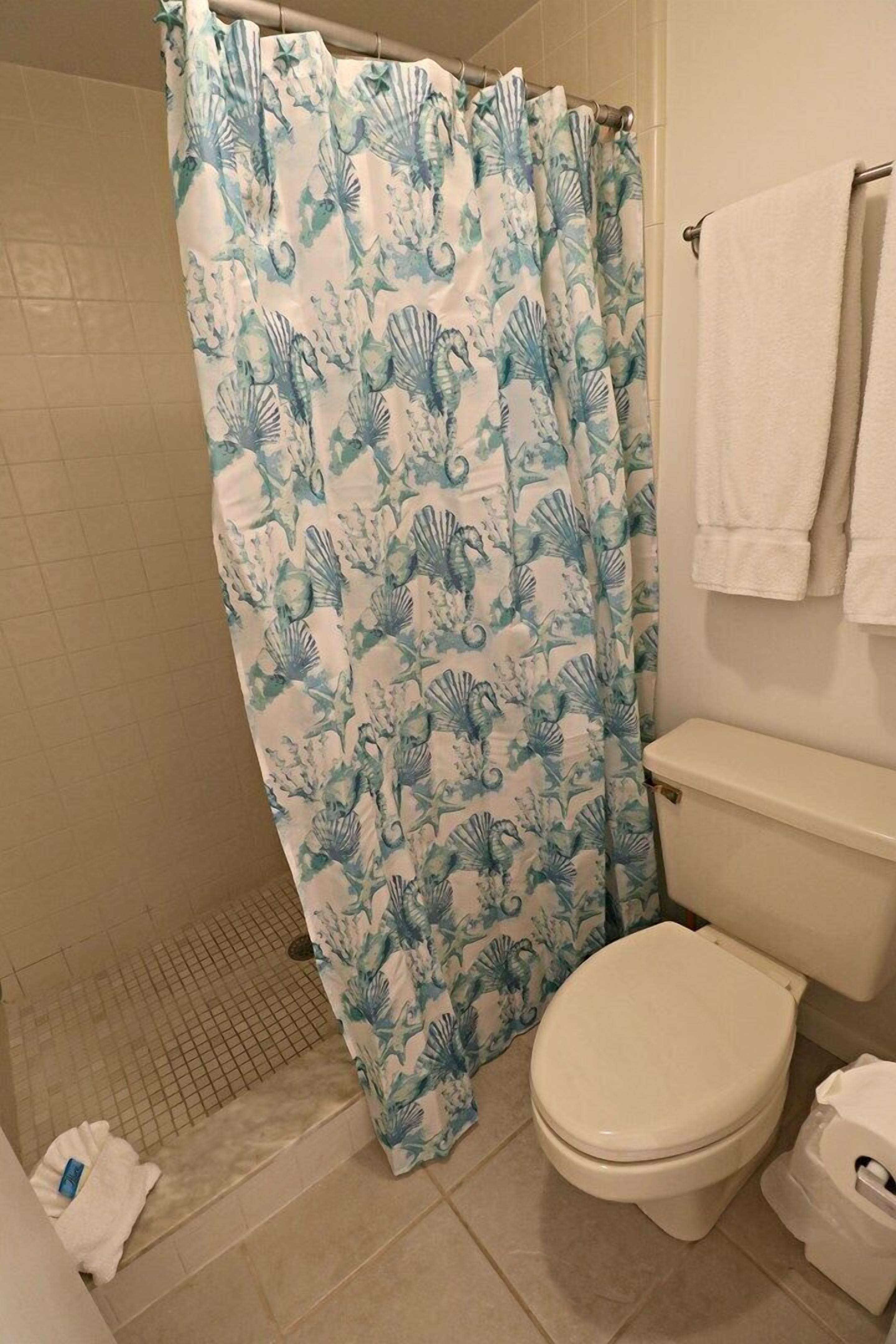 A bathroom with a shower curtain featuring a blue and white floral pattern, a white toilet, and a towel rack with two towels.