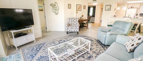 Un salon comprenant un téléviseur, un tapis à motifs, une table basse blanche, un canapé et un fauteuil à motifs.