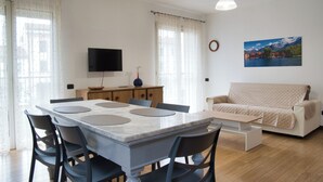 Ett modernt vardagsrum med ett matbord, stolar, en soffa, en platt-TV och en tavla på väggen.
