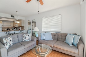 A living room with two sofas, a glass coffee table, and a kitchen in the background. - Ocean Village Club Condo N22 (St. Augustine)