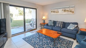 Ein Wohnzimmer mit einer Couch, einem Couchtisch, einem Fernseher und einer Glastür, die auf eine Terrasse führt.