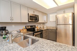 A modern kitchen with stainless steel appliances, granite countertops, and white cabinetry. - Ocean Village Club Condo O16 (St. Augustine)