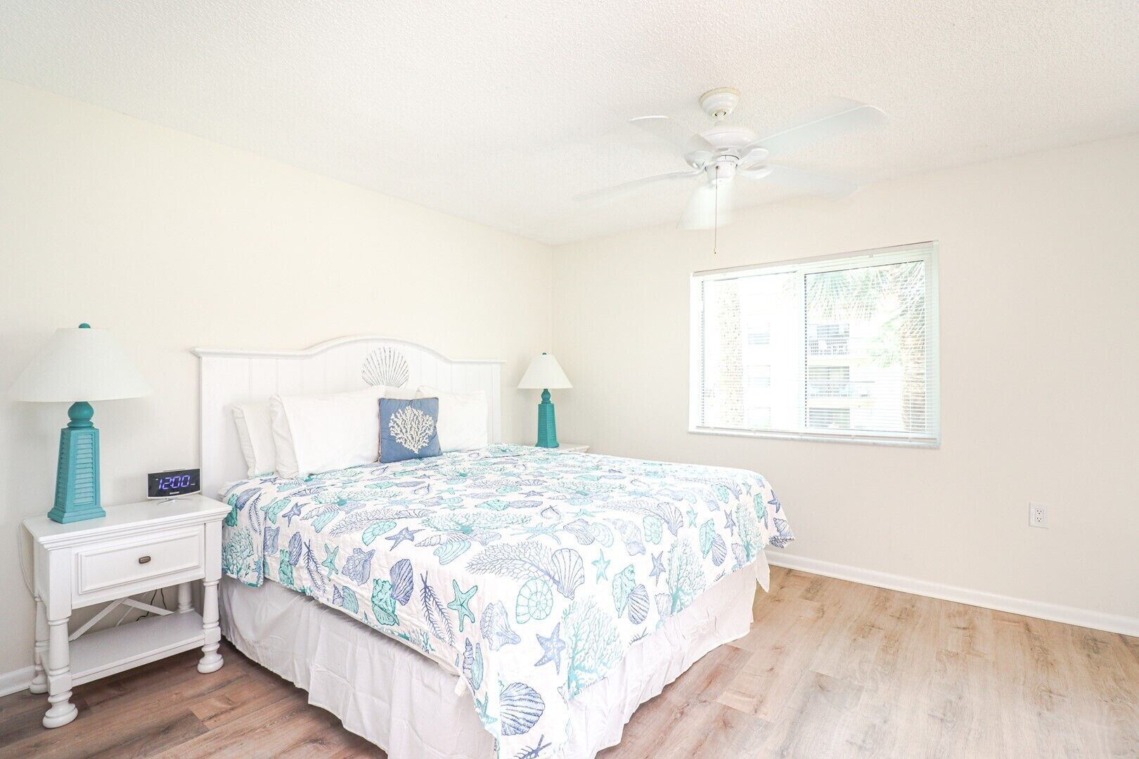 A bedroom with a bed, two nightstands, a ceiling fan, and a window with blinds.